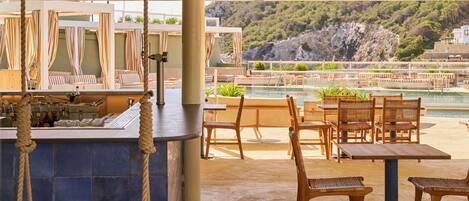 A covered outdoor seating area with a pool view, wooden furniture, and a bar with bottles.