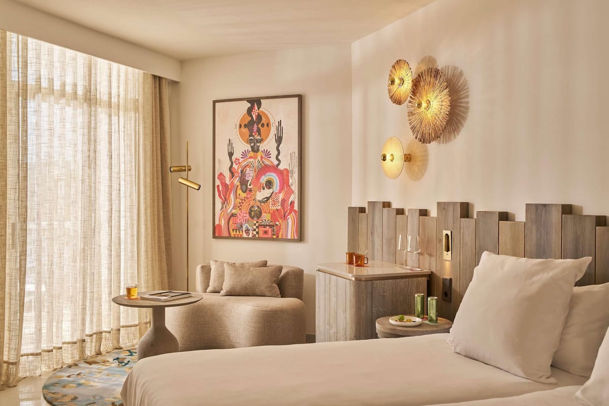 Une chambre d’hôtel moderne avec un grand lit, un petit coin salon, un élément décoratif mural et une table de chevet avec une lampe.