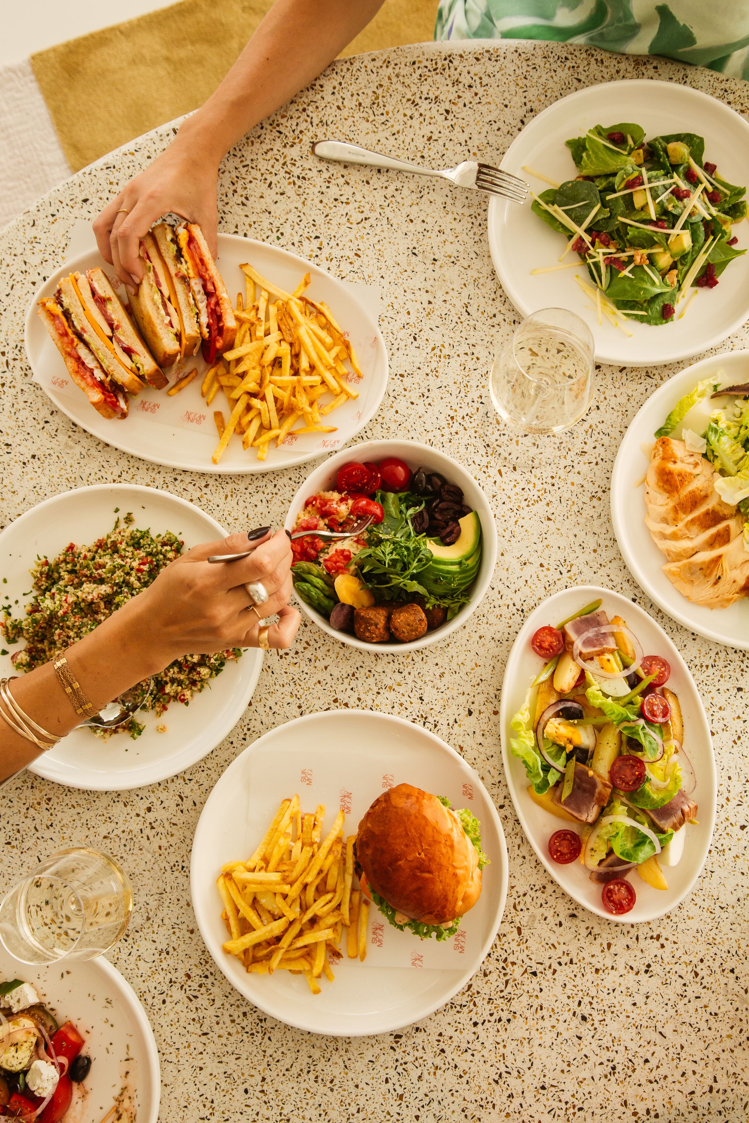 Une table où l’on trouve divers plats, notamment des sandwichs, des salades et des frites.