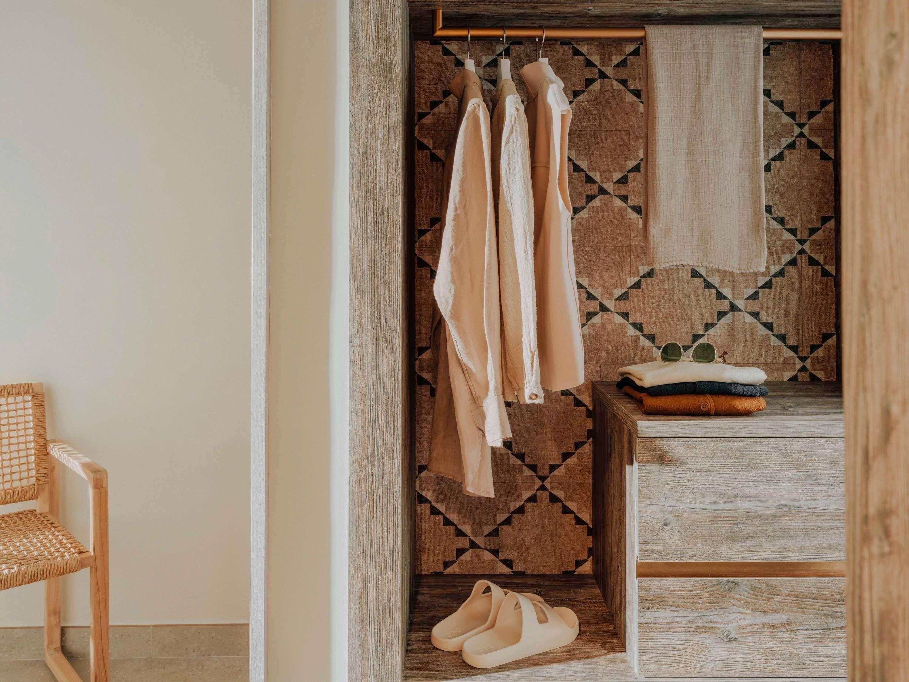 Una stanza con pavimento in legno, una sedia in vimini, una panca di legno e un muro decorato con un motivo geometrico.