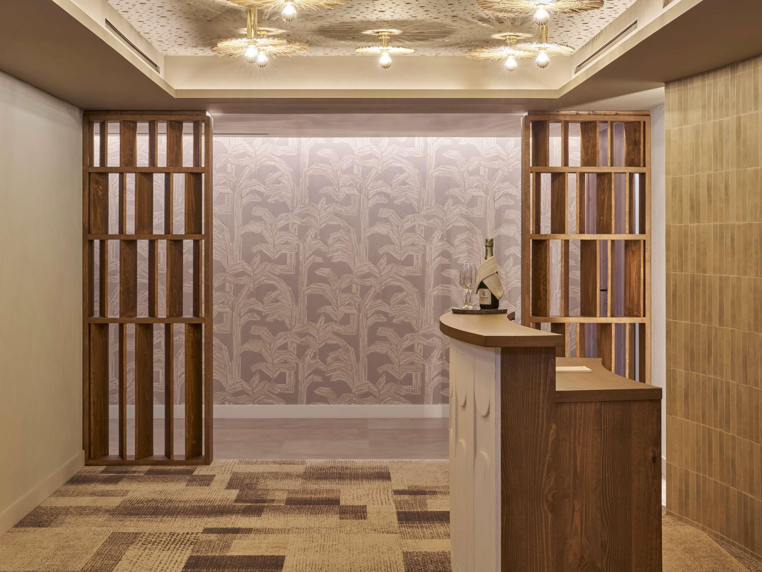 A hallway with a patterned wallpaper, a wooden reception desk, and a ceiling with a geometric light fixture.