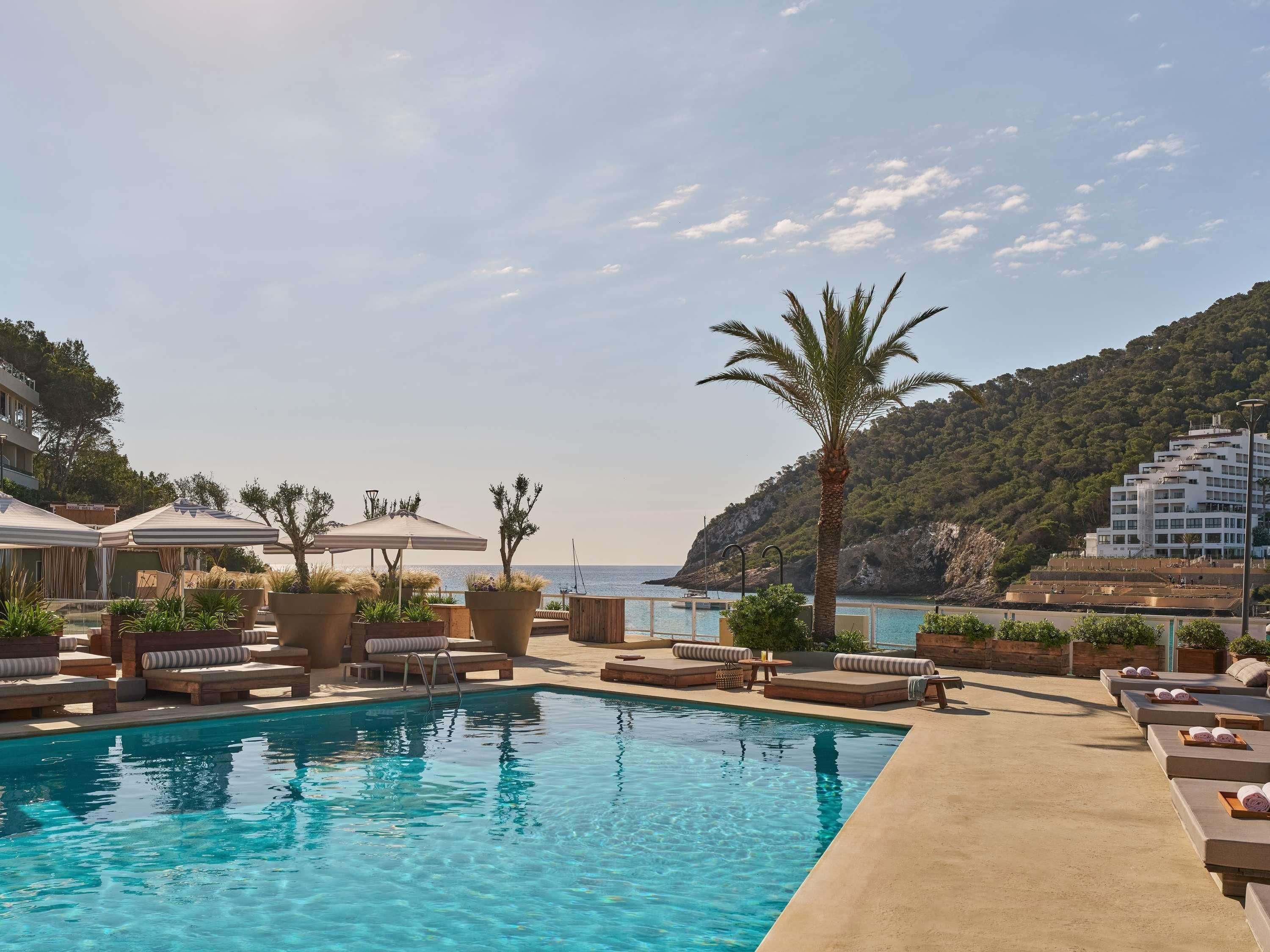 Area piscina con lettini e ombrelloni, una piscina limpida e vista sul mare e sulle colline.