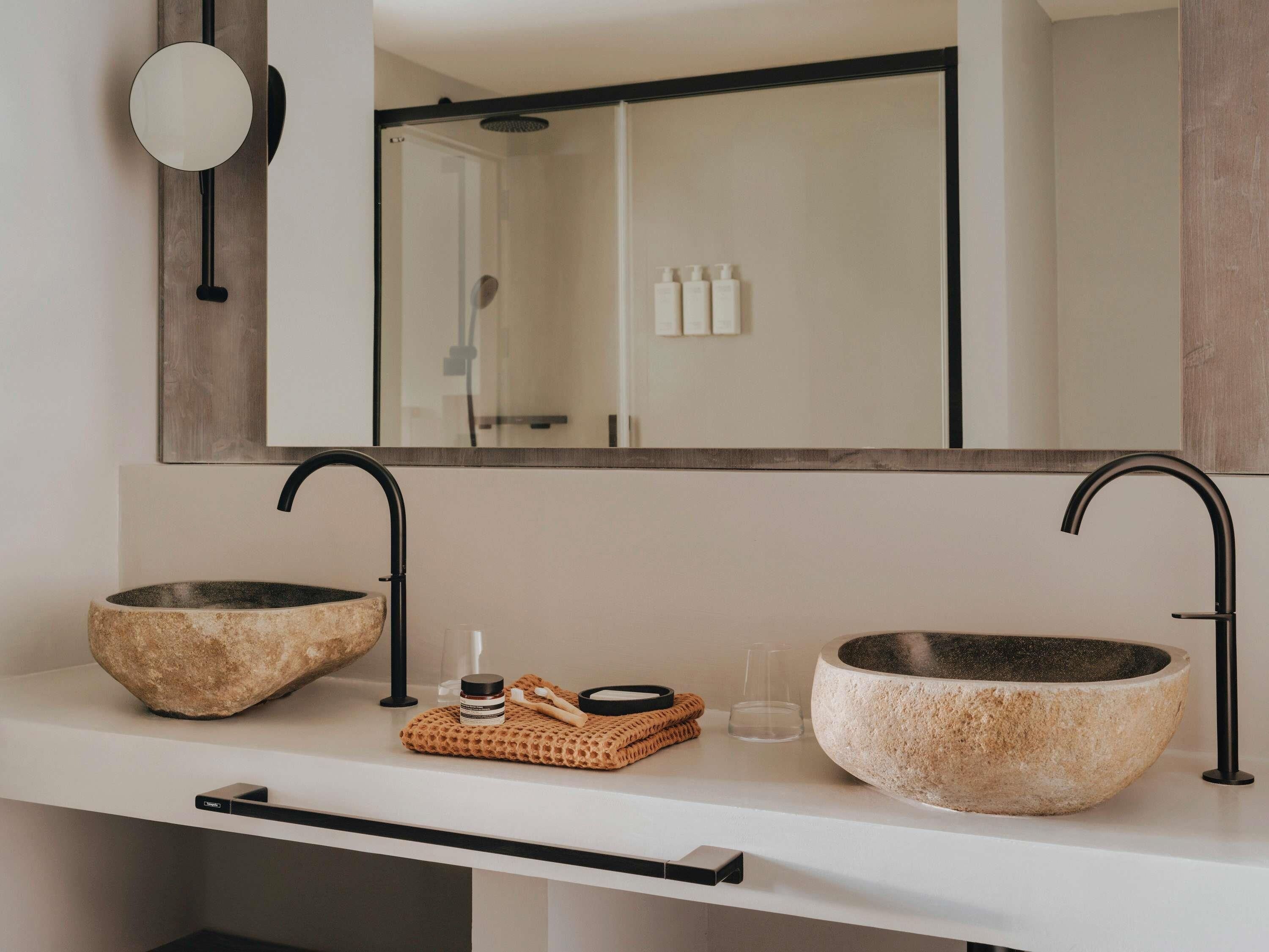 Un bagno con due lavabi in pietra, un porta asciugamani e uno specchio che riflette l'area doccia.