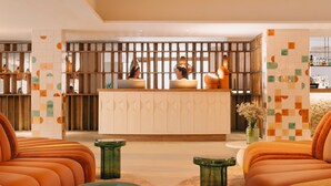 A reception area with a wooden partition, a reception desk, and seating areas with orange sofas and green side tables. - Hyde Ibiza (Santa Eulalia del Rio)