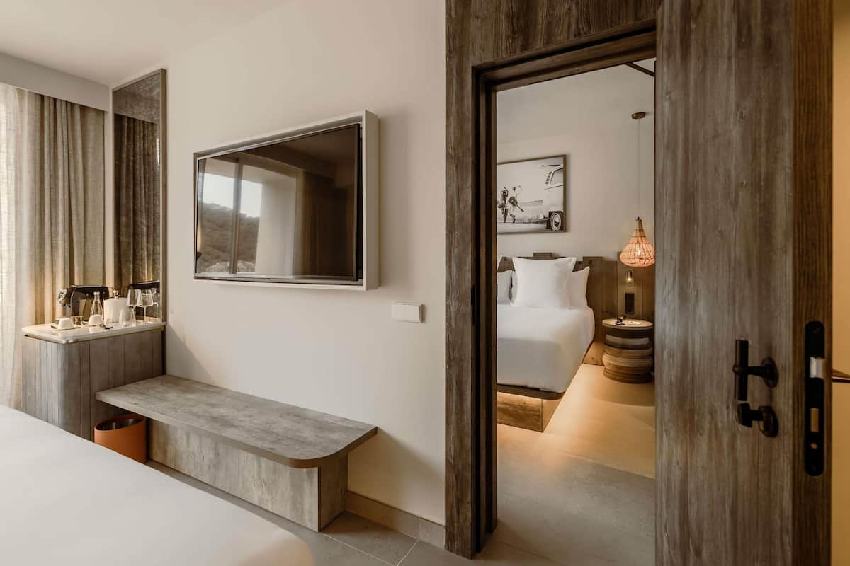 Une chambre d’hôtel moderne, dotée d’un grand miroir, d’une table de chevet, d’un banc et d’un lit avec une petite table à côté.