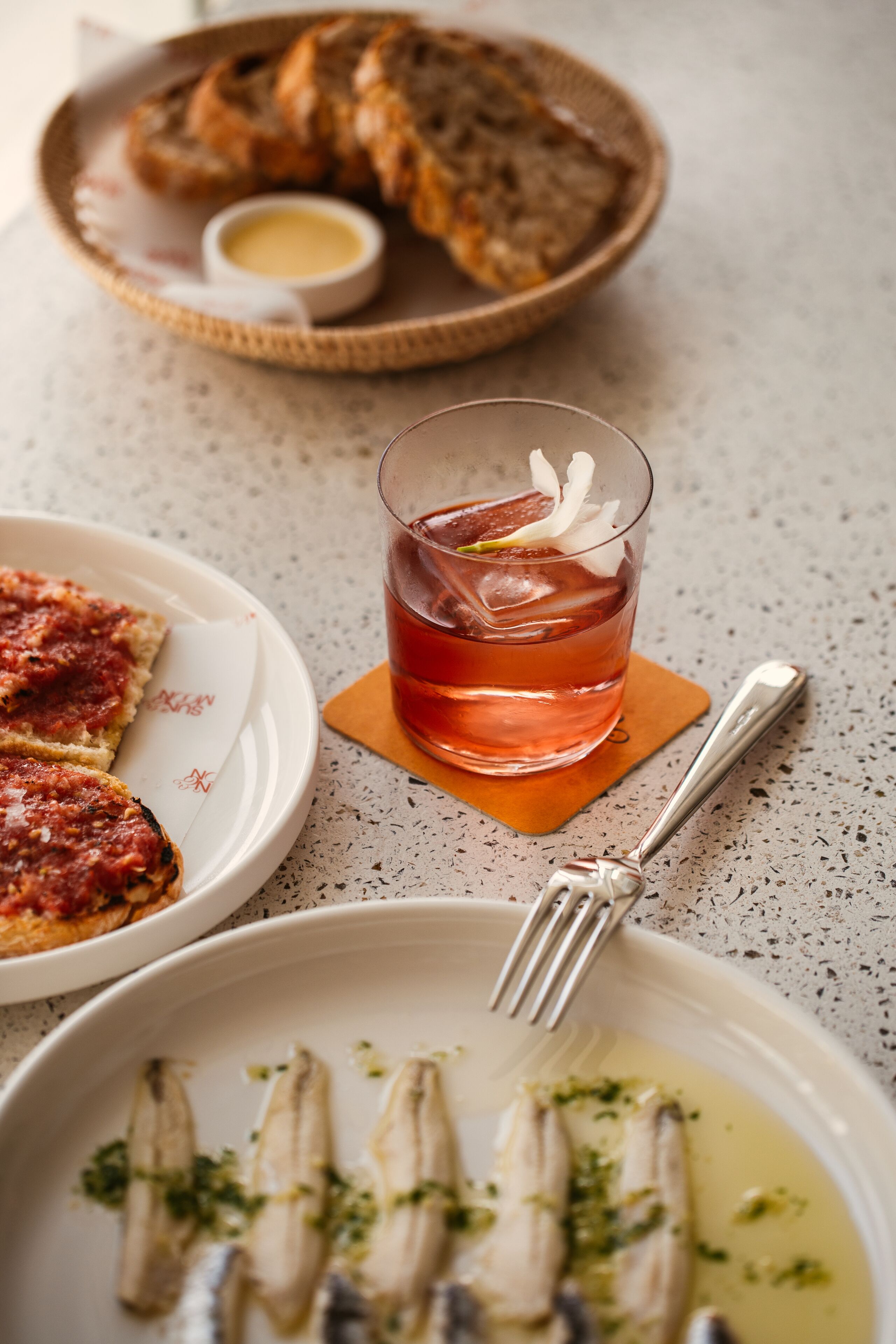A table setting with a plate of bruschetta, a glass of red beverage, and a plate of fish garnished with herbs.
