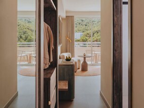 Habitación de hotel con balcón, zona de estar con mesa y sillas, y vistas a un área boscosa.