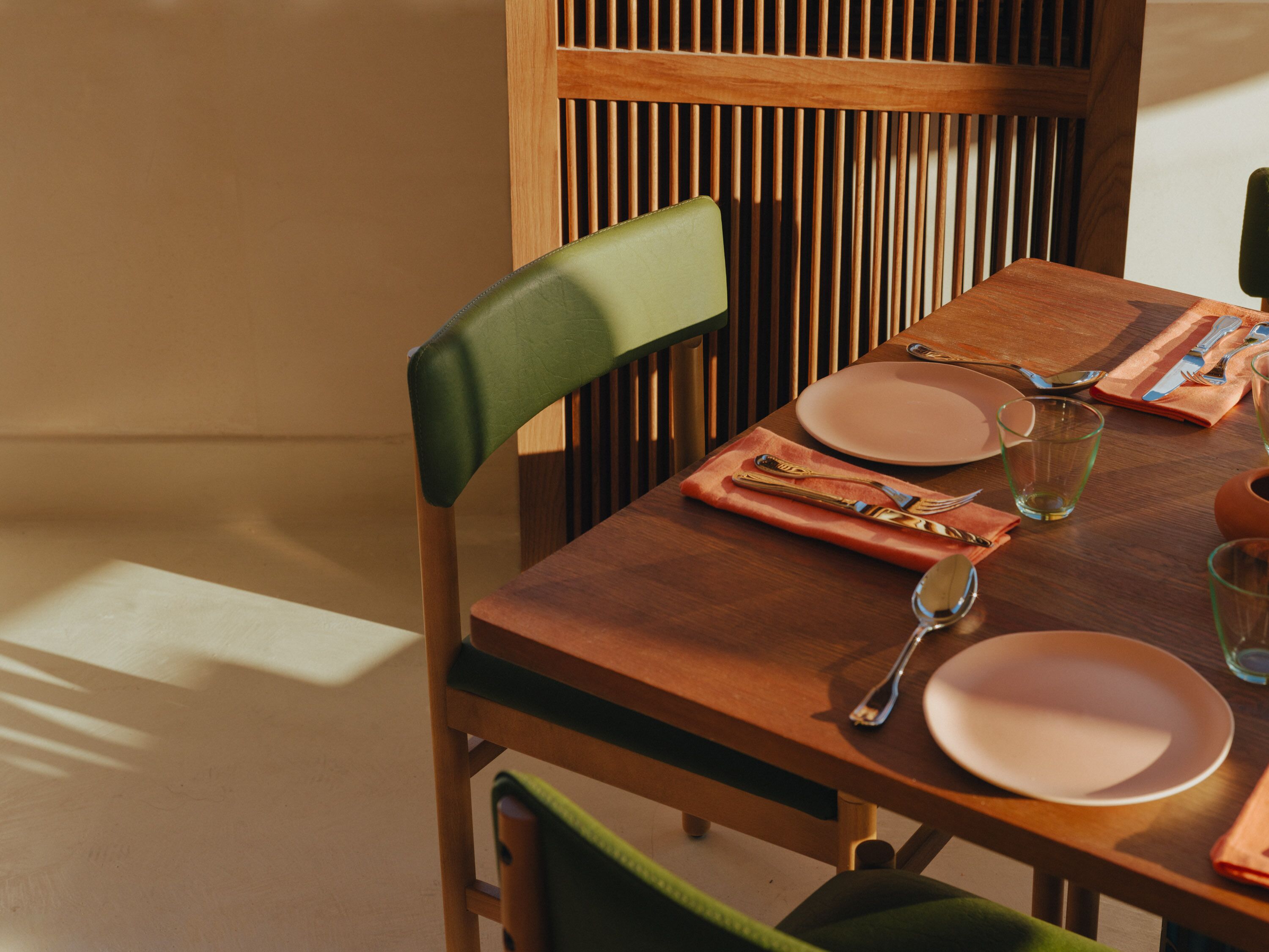 A dining table set with plates, cutlery, and glasses, with a chair and a wooden slat backrest.
