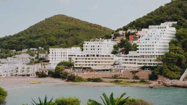 A coastal town with white buildings, a beach, and a hill in the background. - Hyde Ibiza (Santa Eulalia del Rio)