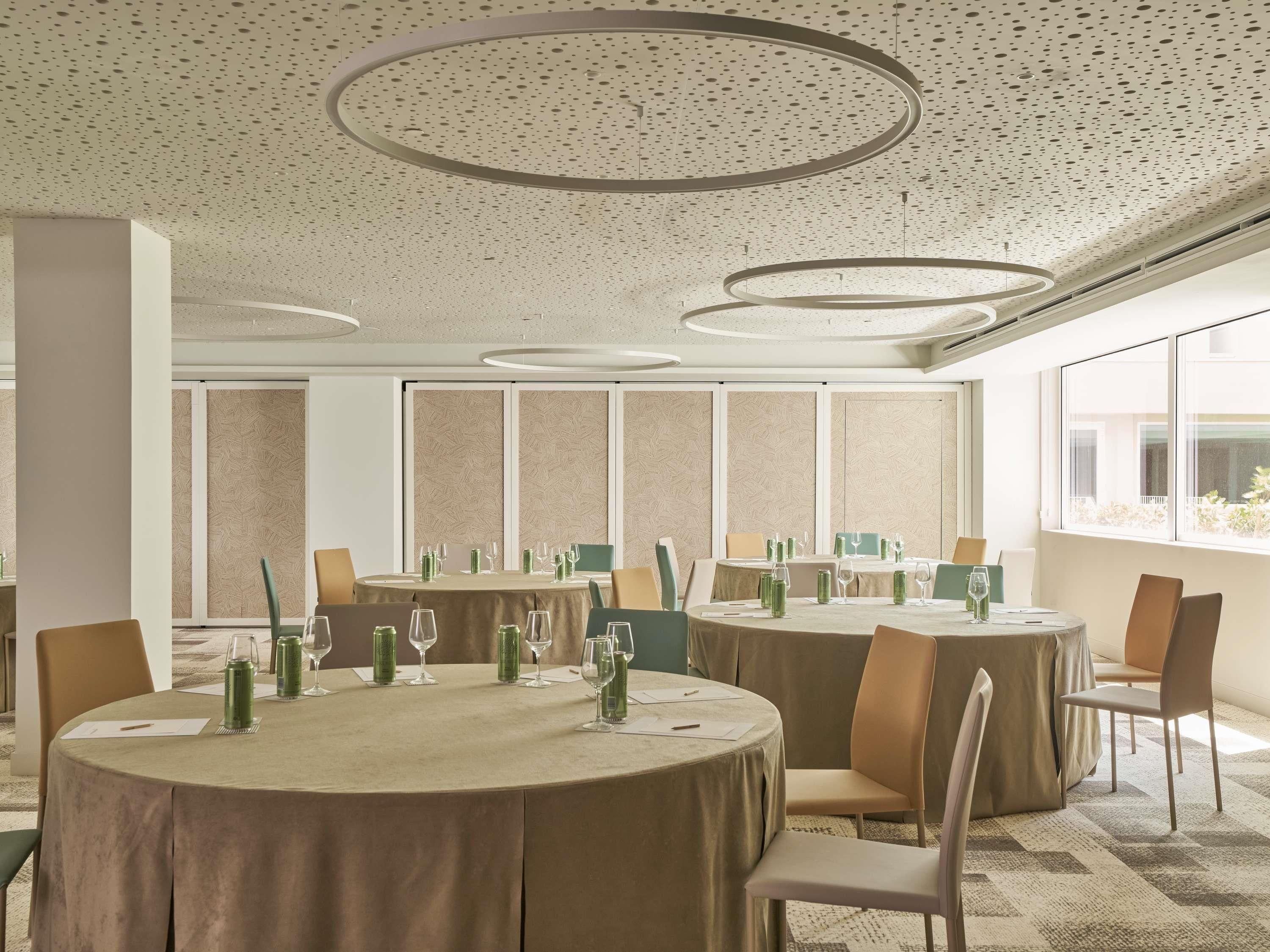 Une salle de conférence avec des tables rondes, des chaises et un mur orné de motifs.