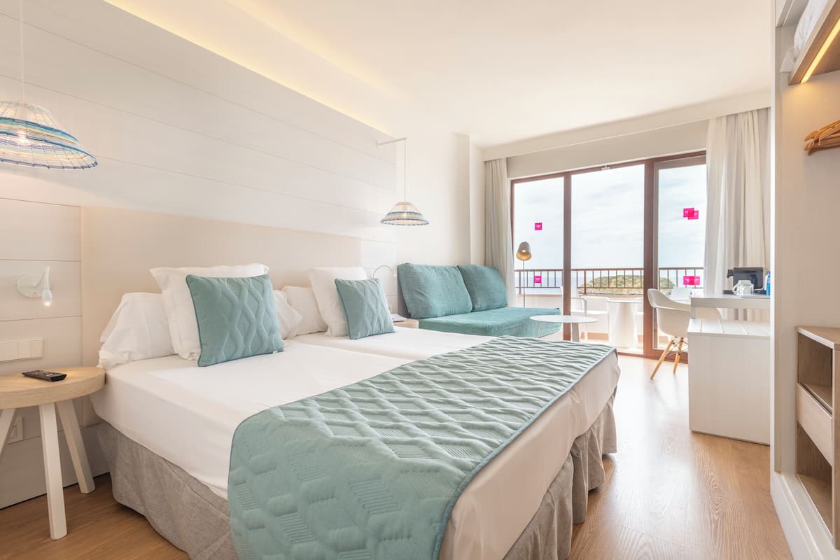 Een hotelkamer met twee bedden, een bureau en een balkon met uitzicht.