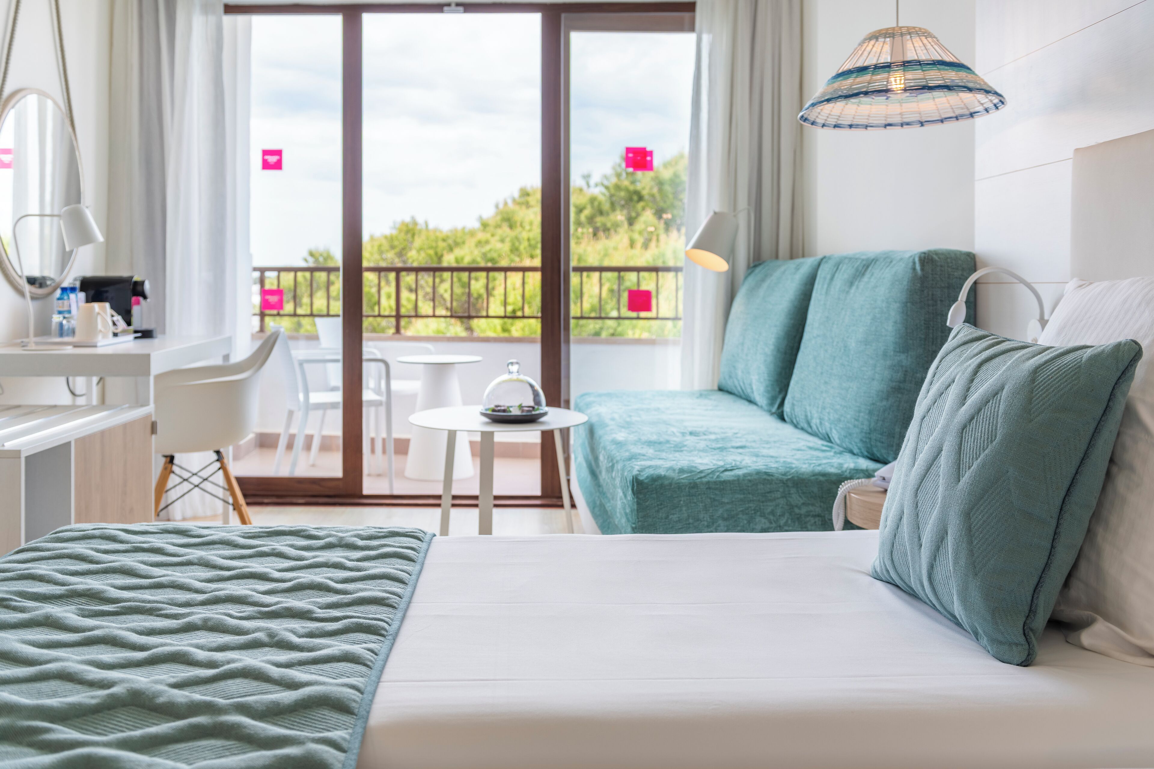 Een slaapkamer met een bed, bureau, stoel, klein tafeltje en balkon met uitzicht.