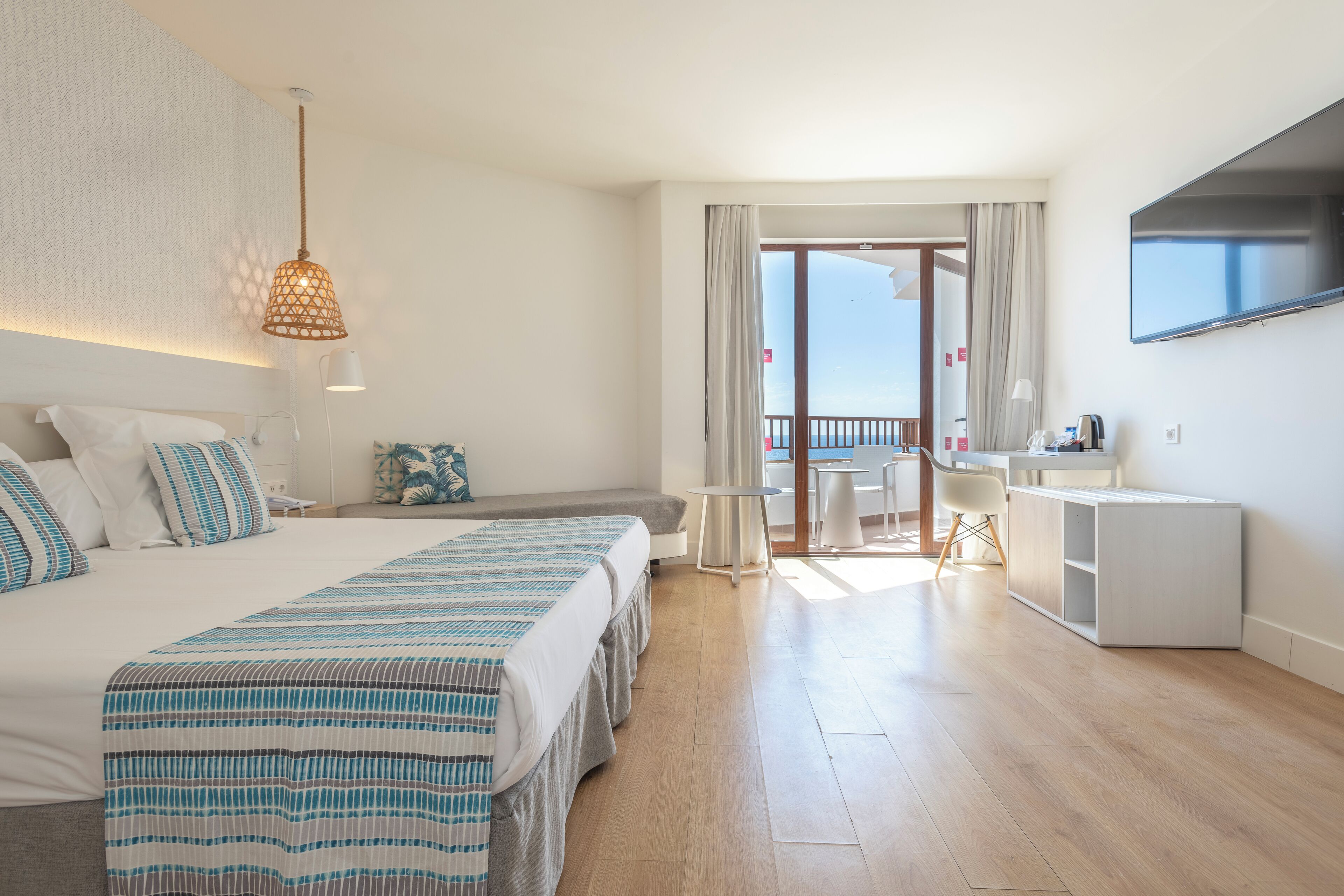 A hotel room with a large bed, a desk, a TV, and a balcony with curtains.