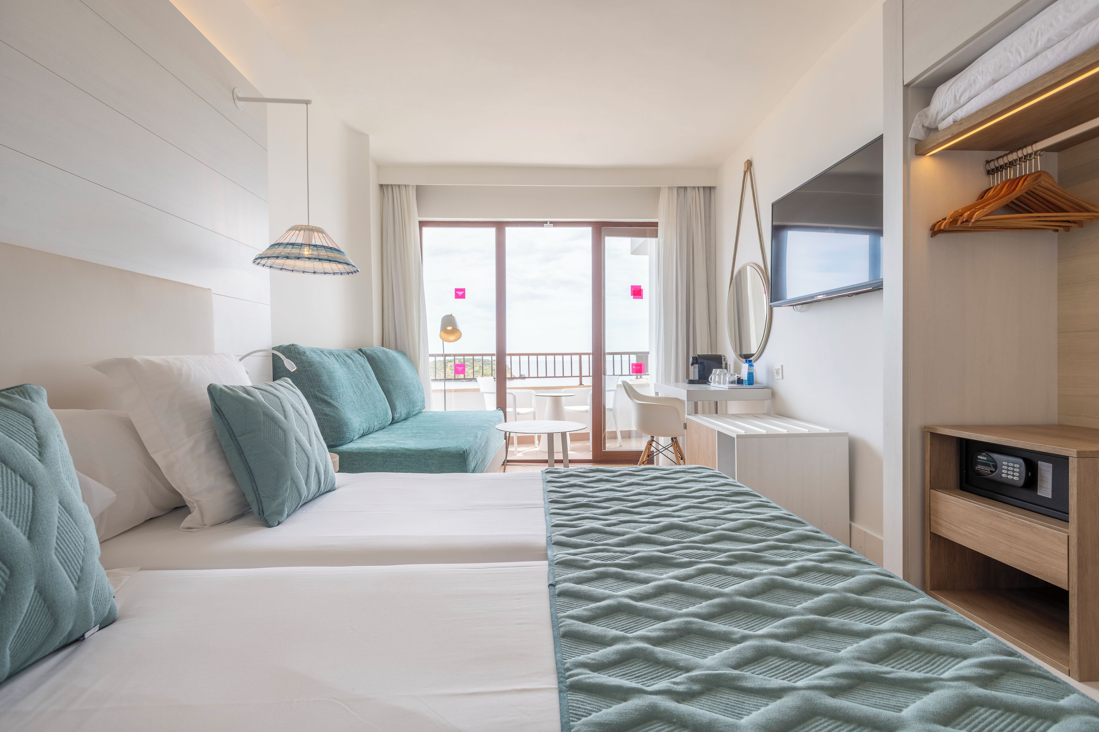 Une chambre d’hôtel comprenant un lit, un bureau, une chaise, une télévision et un balcon avec une table et des chaises.
