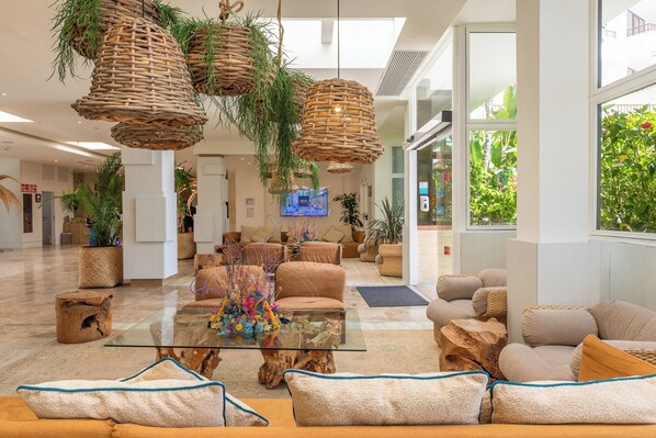 A spacious lobby with wicker hanging lamps, comfortable seating, a glass coffee table, and large windows offering views of greenery outside. - Leonardo Royal Ibiza Santa Eulalia (Santa Eulalia del Rio)