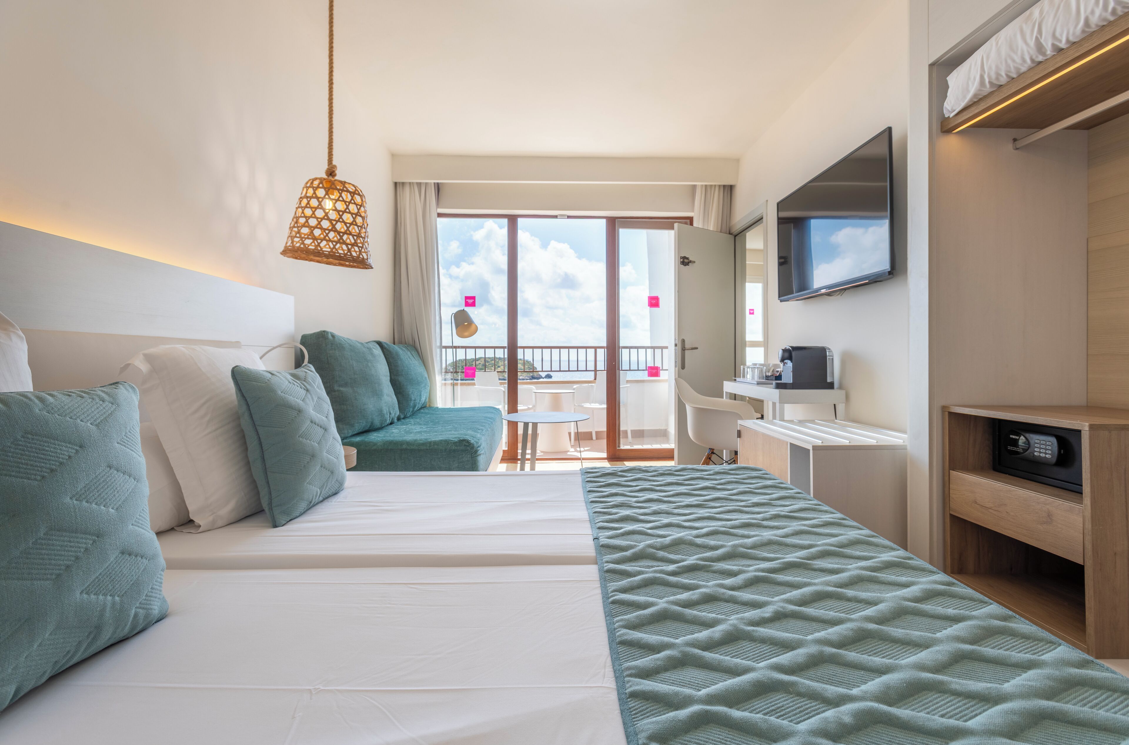 Habitación de hotel con cama, escritorio, silla, televisor y balcón con vistas.