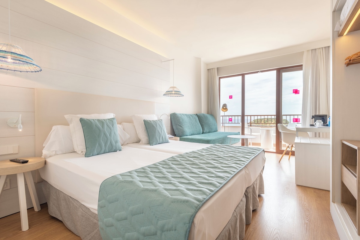 A hotel room with two beds, a desk, and a balcony with a view.