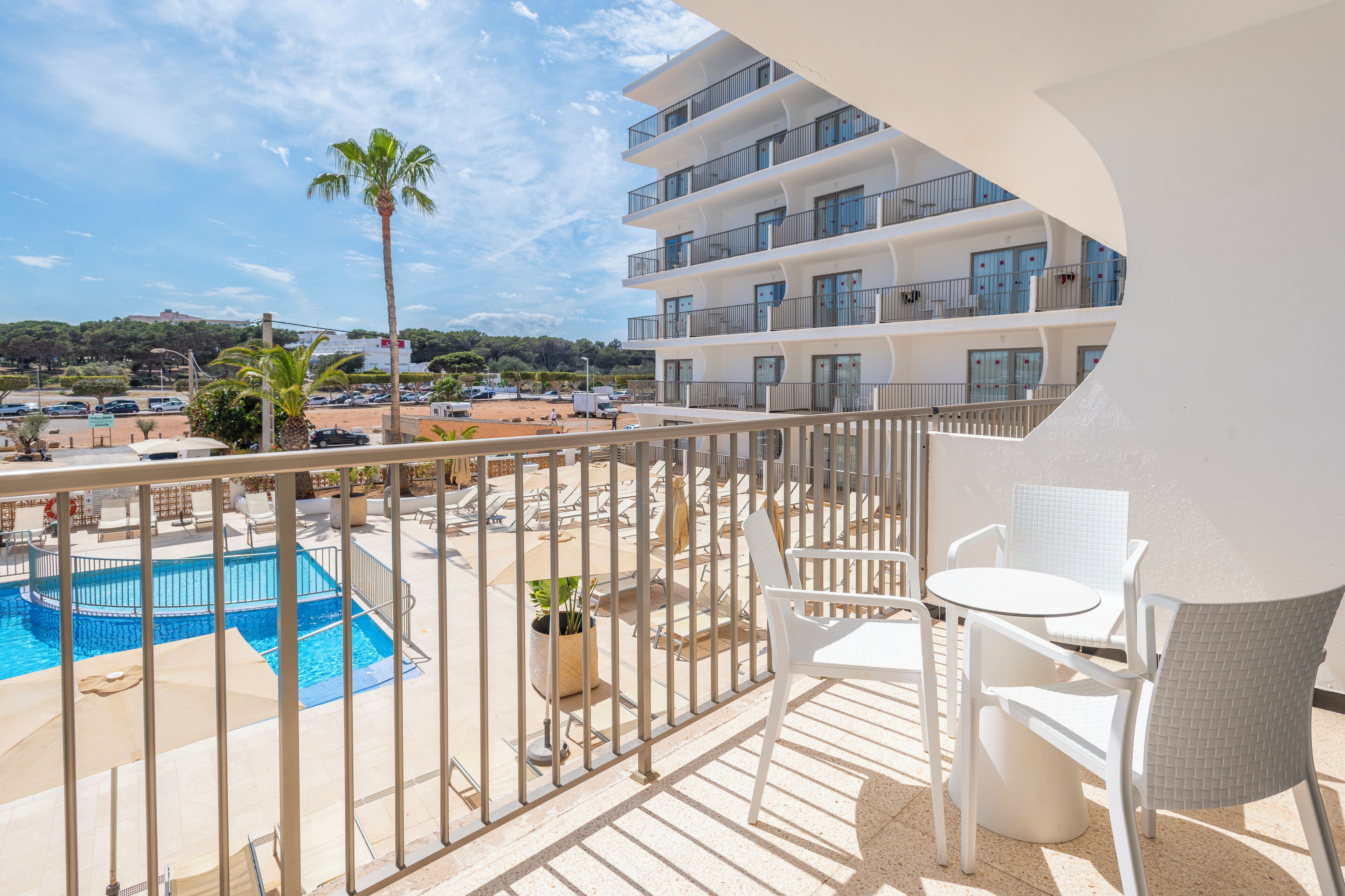 A balcony with a pool, white furniture, and a view of a building and beach.