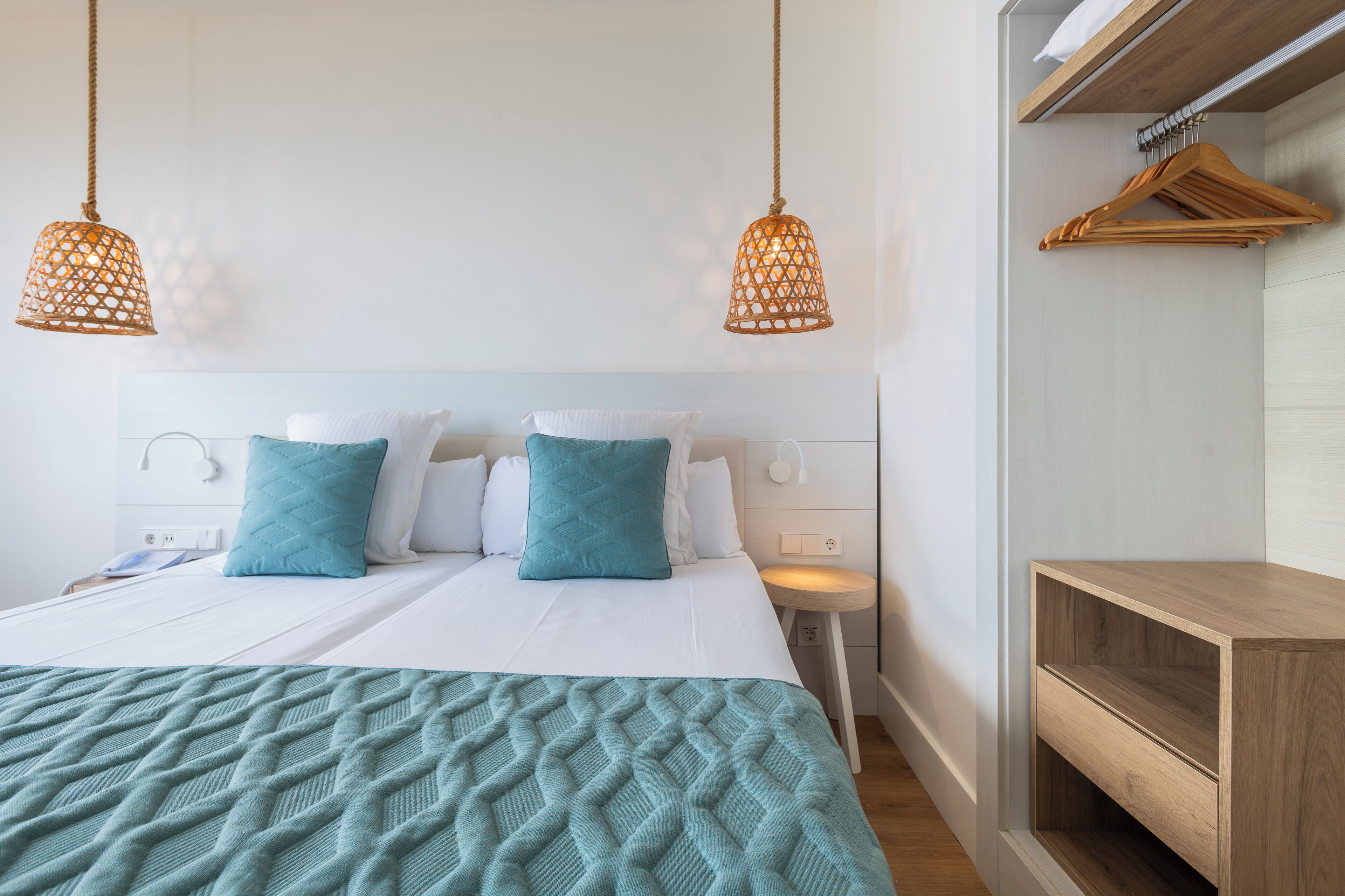 Un dormitorio ordenado con cama, dos mesitas de noche, una lámpara colgante y un estante de madera.