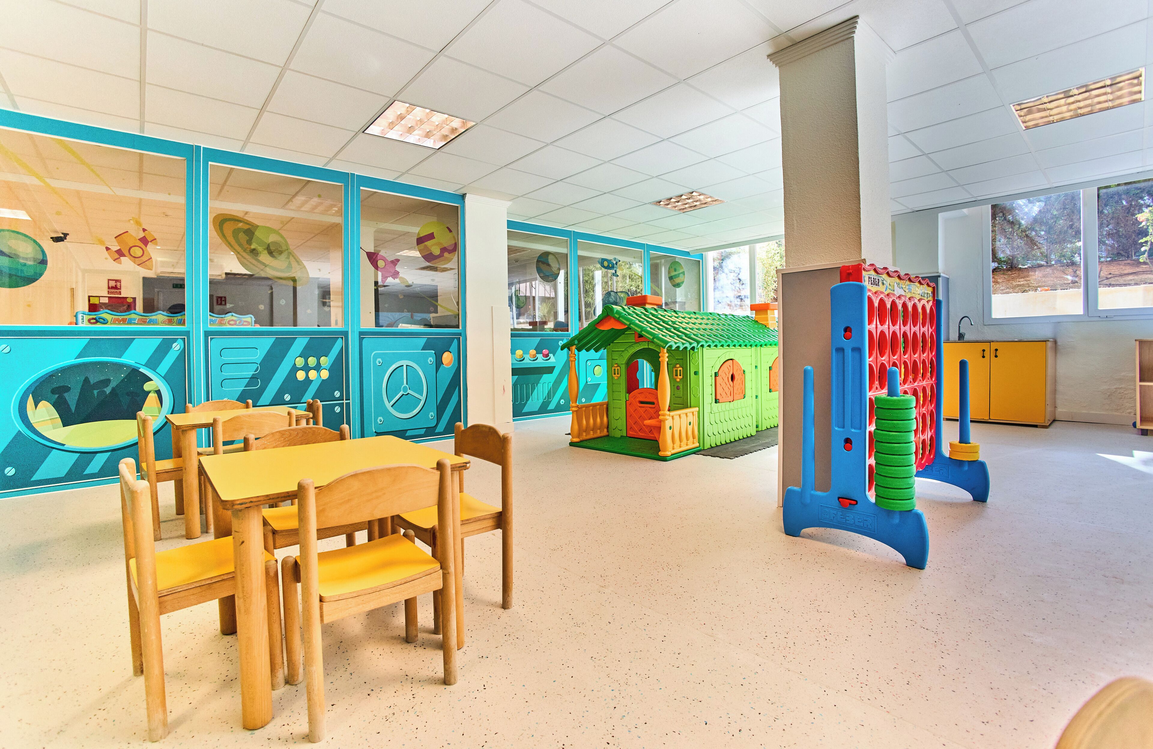 A classroom with a play area, wooden tables, and chairs.
