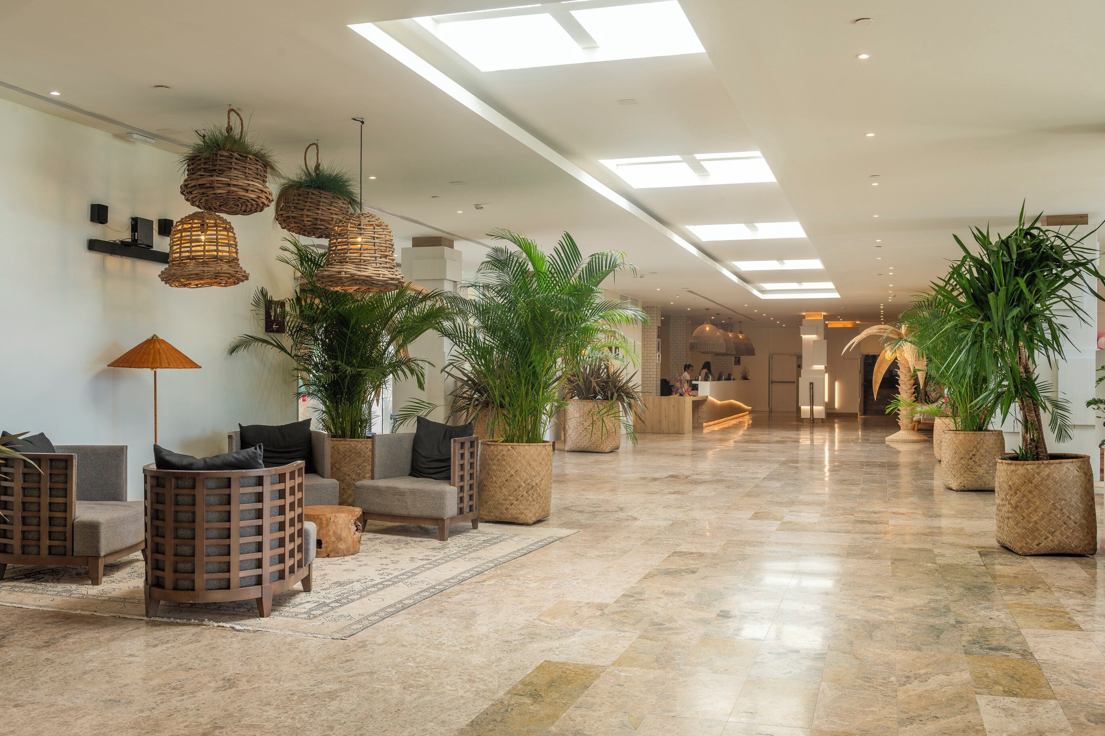 A spacious lobby with a polished marble floor, wicker hanging lamps, and several potted plants.