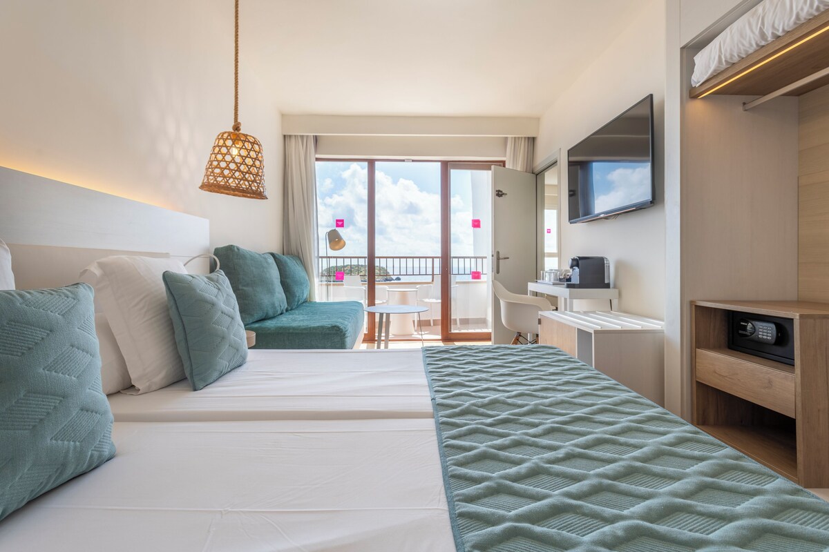 A hotel room with a bed, a desk, a chair, a TV, and a balcony with a view.