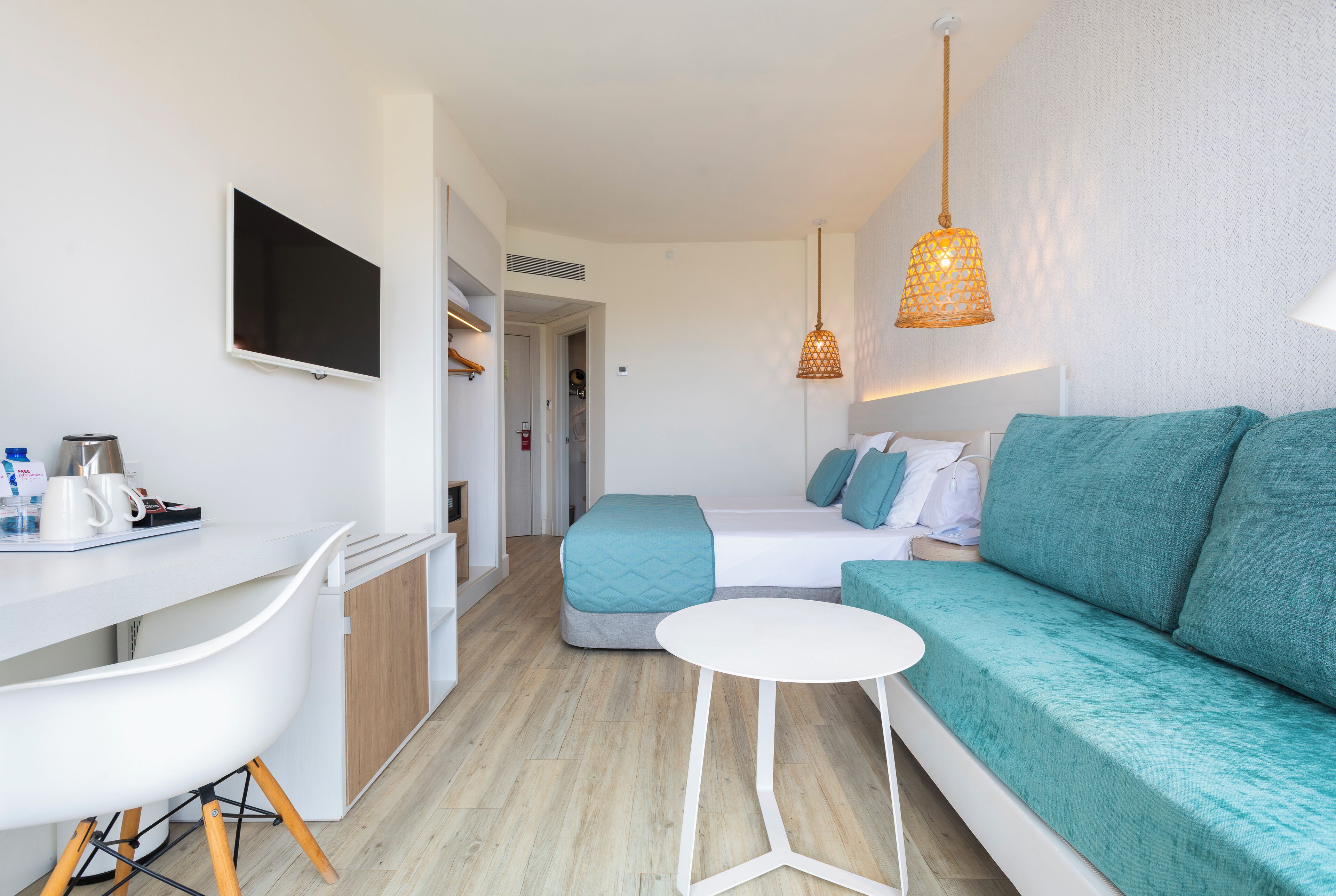 Una habitación de hotel moderna con un escritorio blanco, un sofá verde azulado y una pequeña mesa blanca.