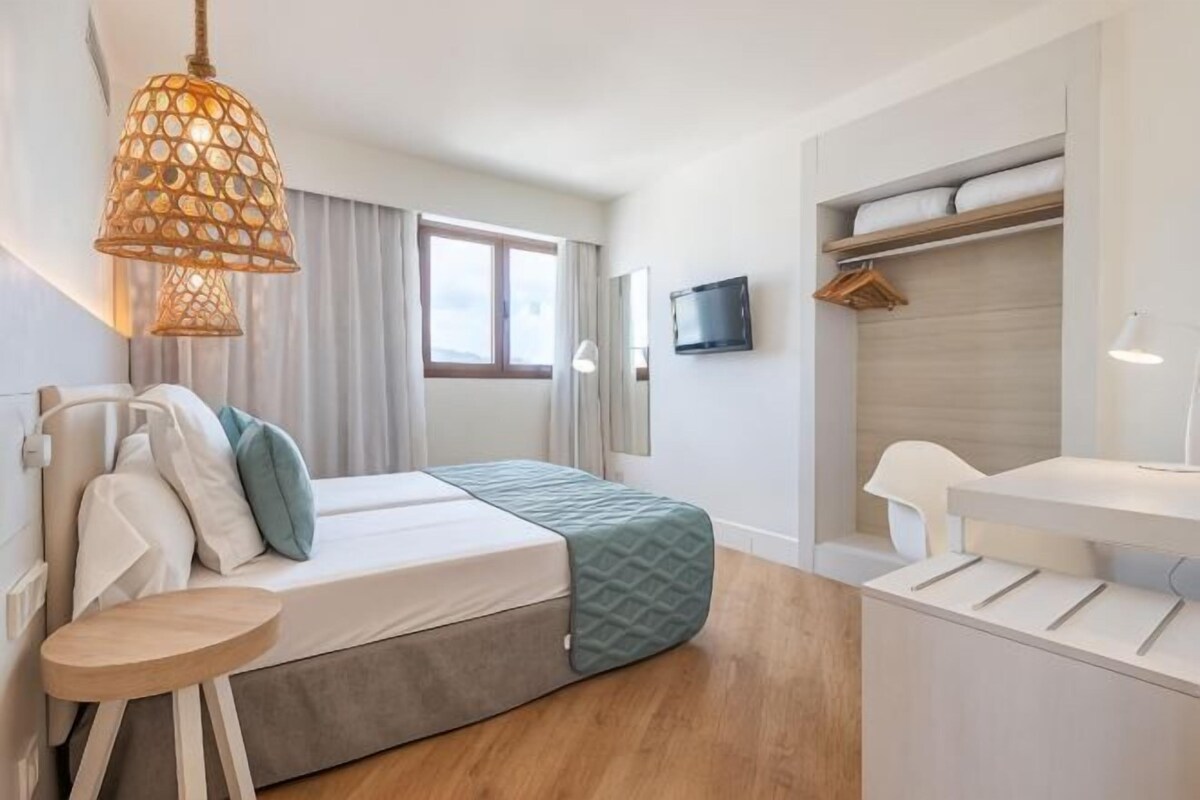 A bedroom with a bed, bedside table, lamp, and a TV on the wall.