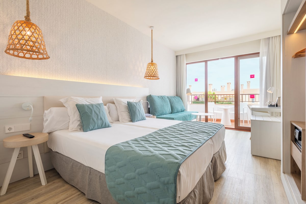 Een moderne hotelkamer met een groot bed, een bureau en een balkon met zitplaatsen.