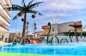 A swimming pool with water features, palm trees, and a slide.