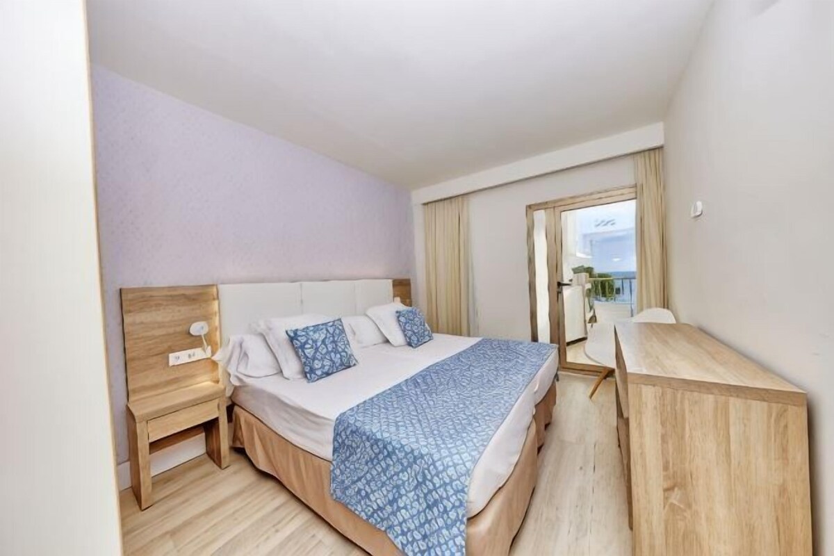 A bedroom with a bed, bedside tables, a desk, and a window with curtains.