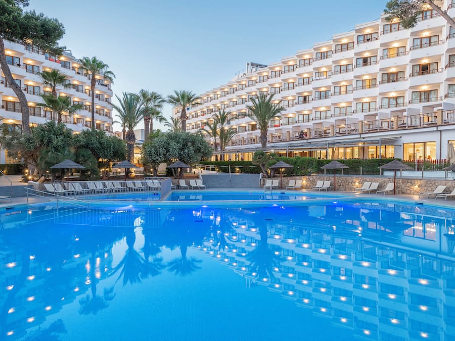 Un hotel con una amplia piscina al aire libre, varios balcones y palmeras.