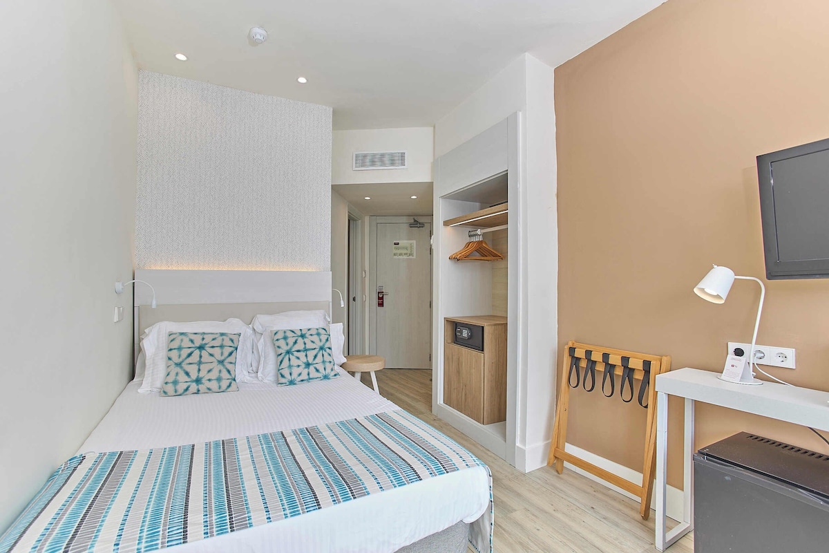 A bedroom with a bed, bedside table, desk, and a TV.