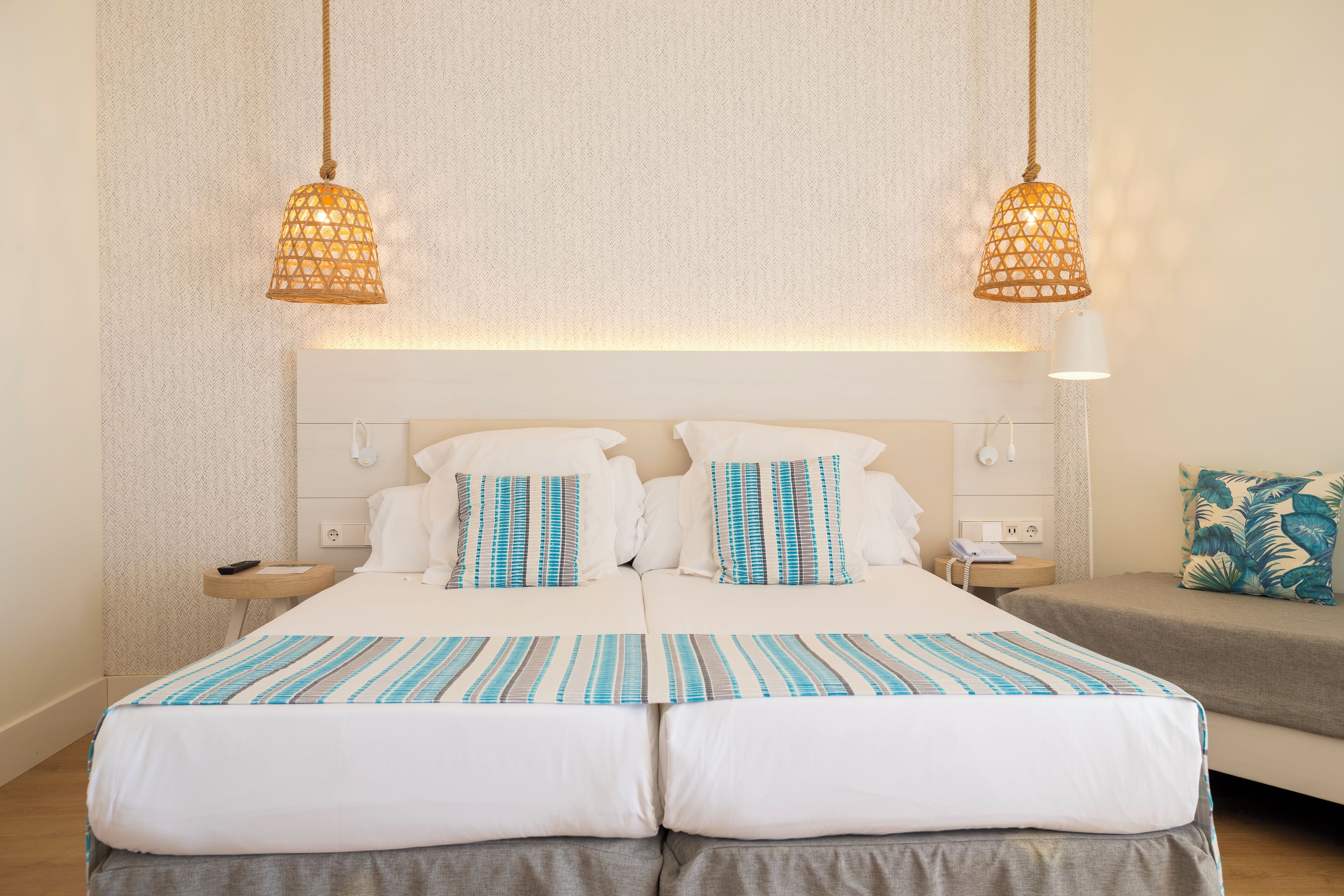 Una cama doble con ropa de cama a rayas blancas y azules, dos mesitas de noche con lámparas y un tocador con un teléfono.