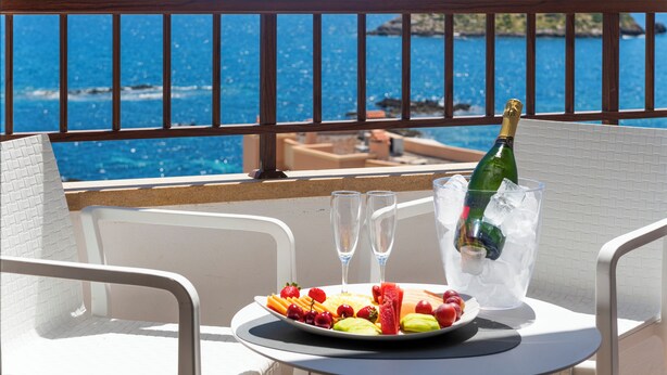 Un balcon avec une table dressée pour deux personnes, une assiette de fruits, deux verres et une bouteille de champagne dans un seau à glace.