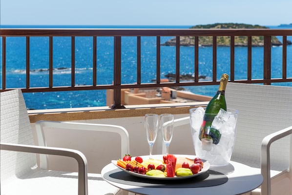 A balcony with a table set for two, a plate of fruit, two glasses, and a bottle of champagne in ice.