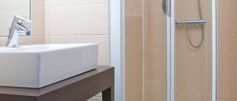 Un baño con un lavamanos blanco, ducha con cerramiento de vidrio y un inodoro.