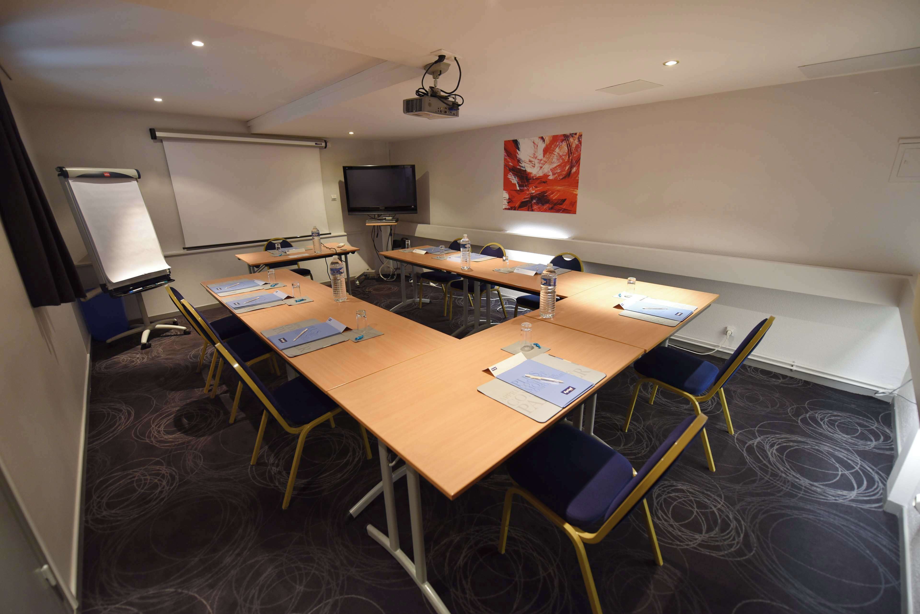 A conference room with a long table, chairs, a projector, a screen, and a television.