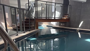 Una piscina interior con barrera de vidrio, una escalera y un cartel que indica una profundidad de 1.8 metros.