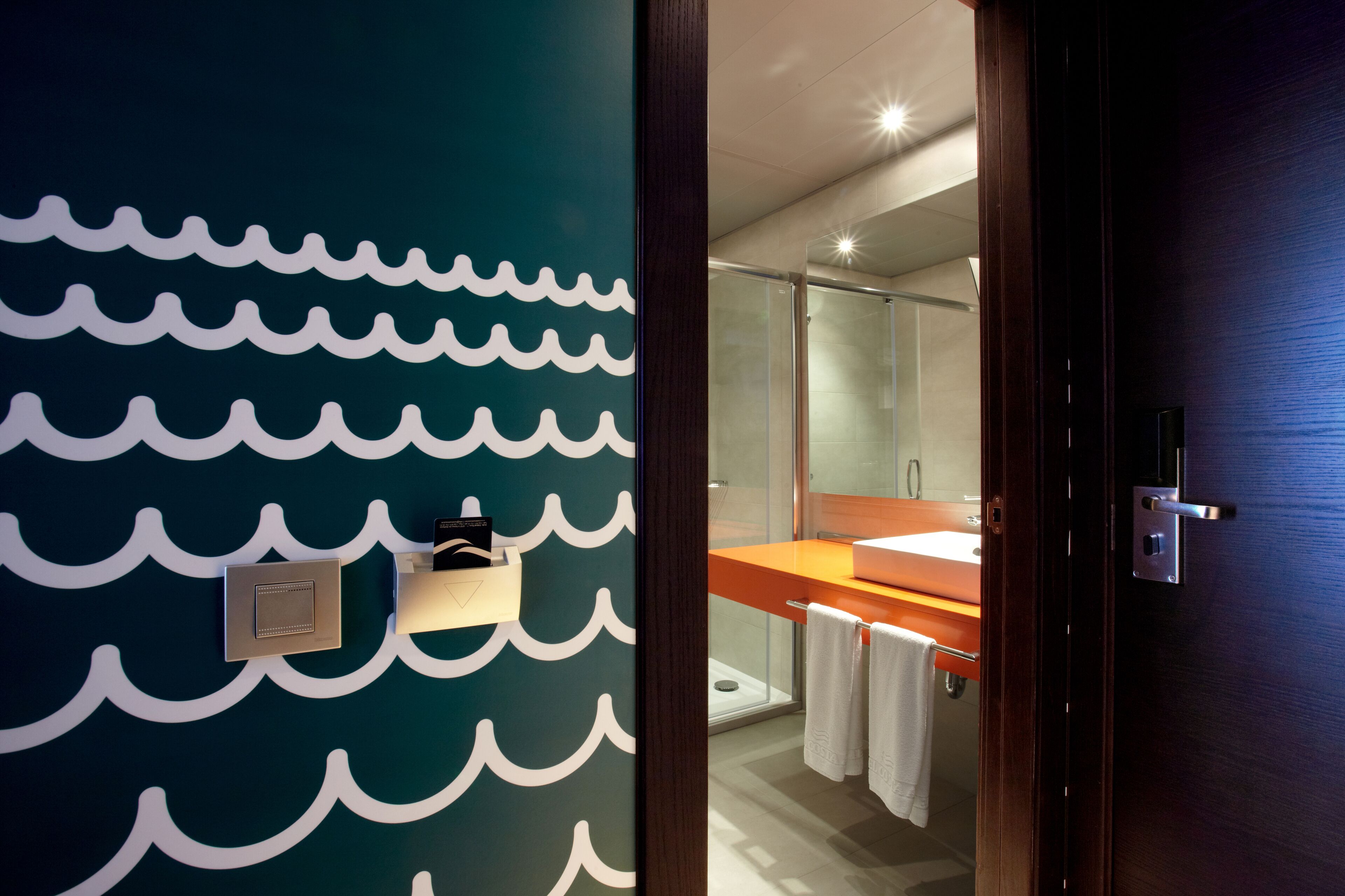 A modern bathroom with a wave-patterned wall, a glass shower enclosure, and a wooden door.