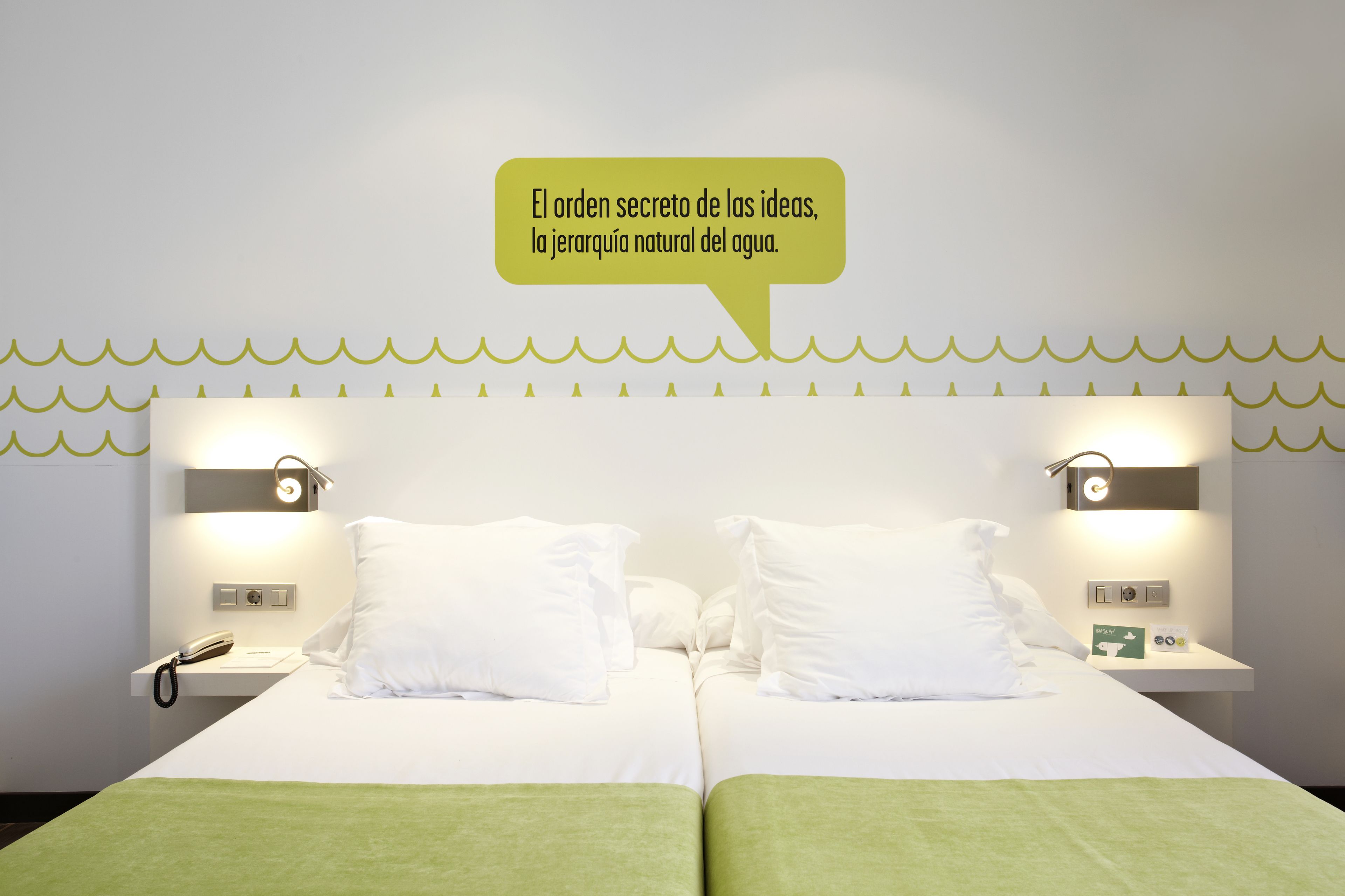 A hotel room with two beds, nightstands, a phone, and a wall-mounted light fixture.