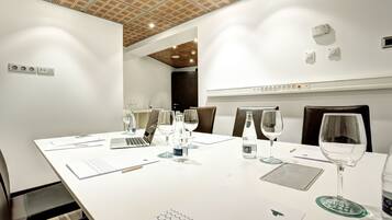 A modern conference room with a white table, laptops, glassware, and a wooden ceiling.