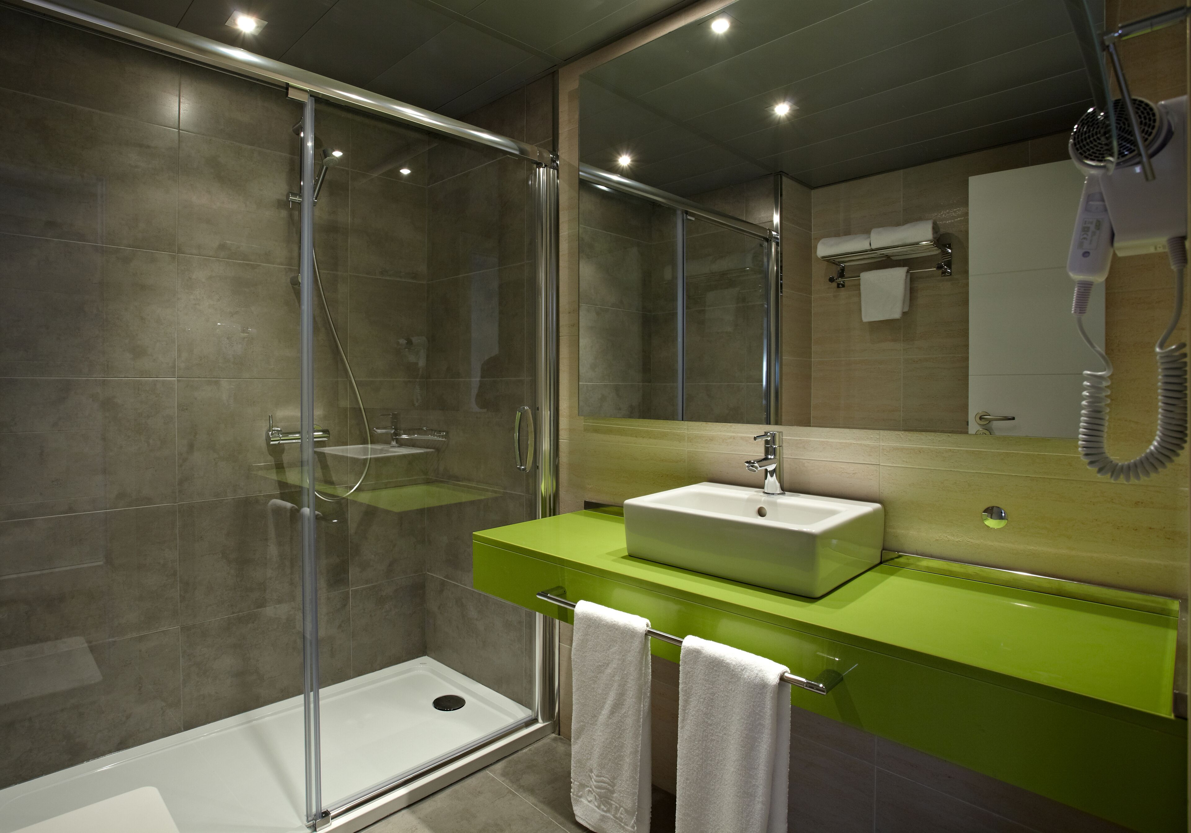 A modern bathroom with a glass shower enclosure, a green vanity, and a large mirror.