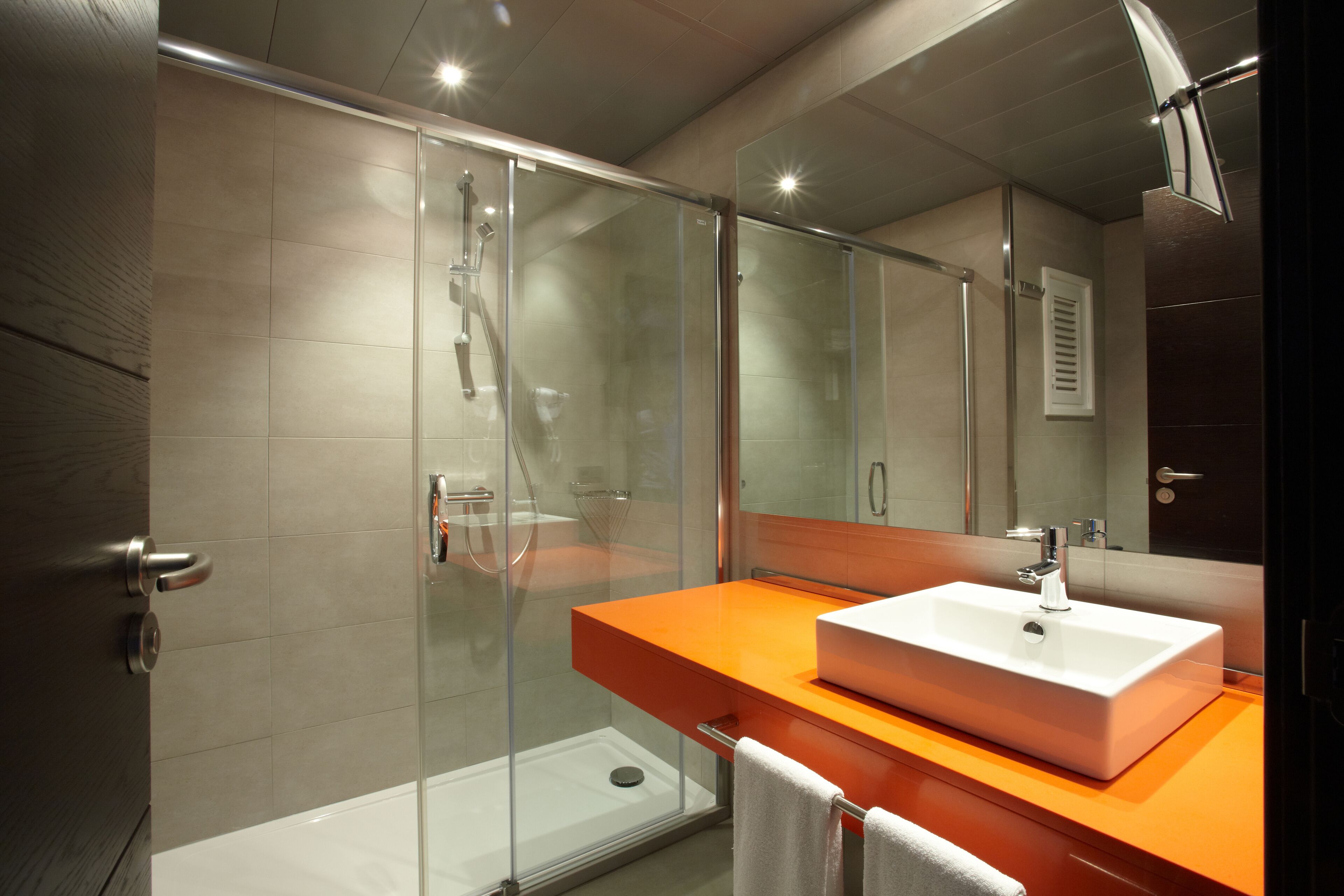 A modern bathroom with a glass-enclosed shower, a white sink, and an orange countertop.
