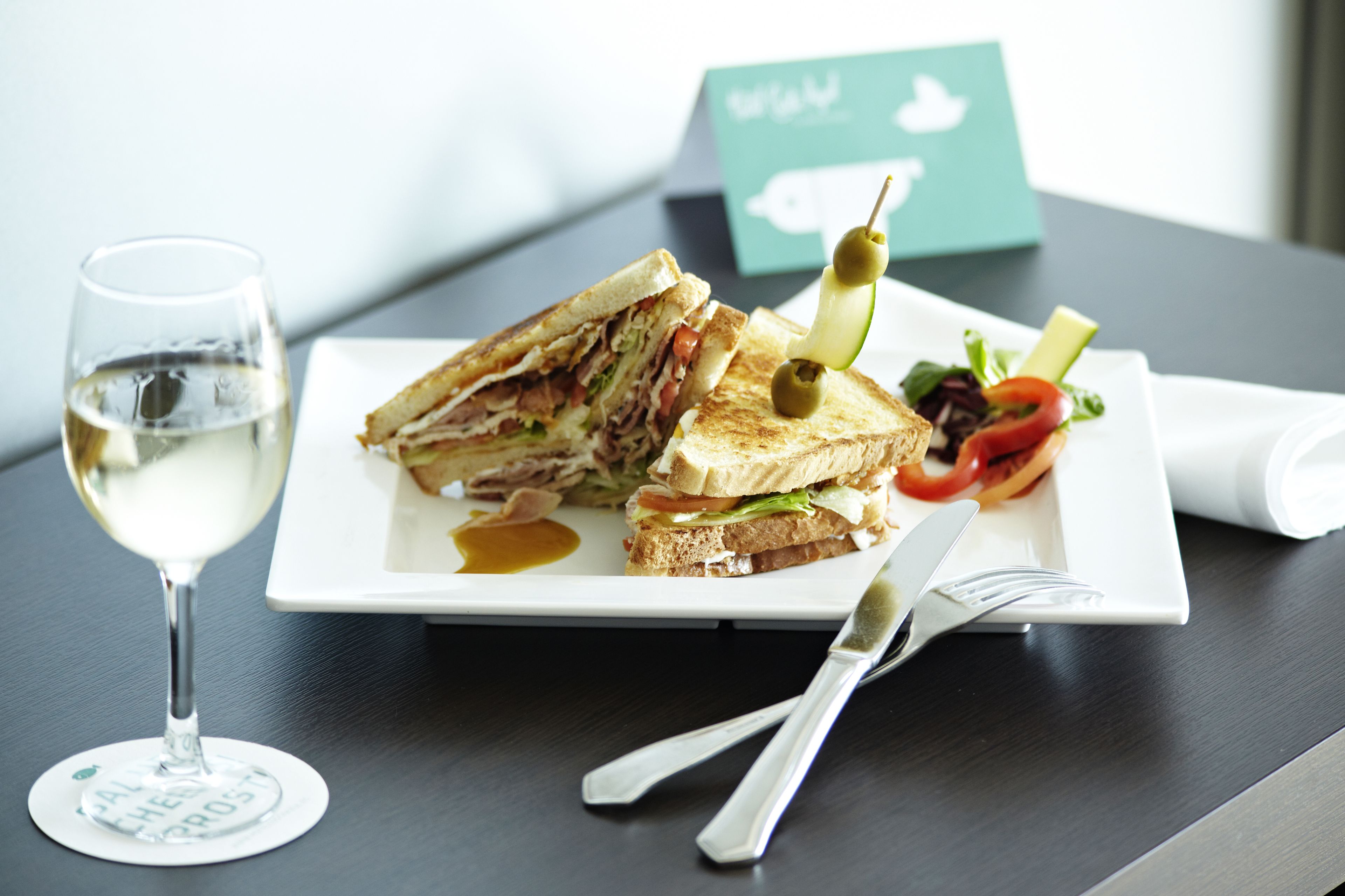 Un sandwich accompagné d’une salade et d’un verre de vin blanc, le tout servi sur une assiette.