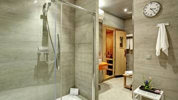 A modern bathroom with a glass-enclosed shower, a visible clock, and a small table with a tray.
