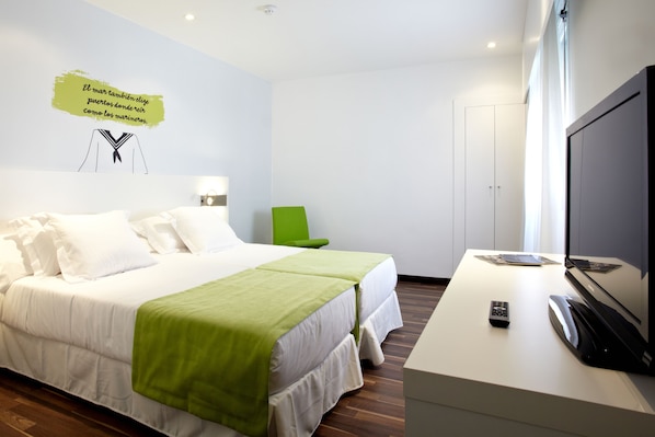 Habitación de hotel con cama, escritorio con televisor, silla verde y pared con una cita.