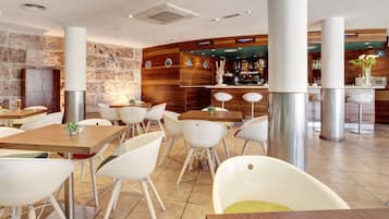 A modern restaurant with white chairs and tables, a stone wall, and a bar area.