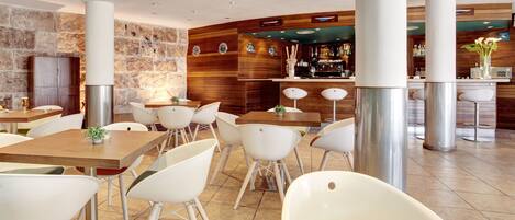 Un restaurante moderno con sillas y mesas blancas, una pared de piedra y una zona de bar.