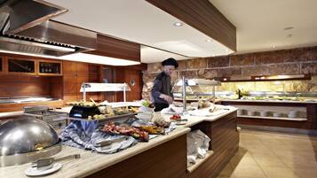 A buffet setup with various food items, a chef preparing food, and a modern kitchen with wooden cabinets and stone accents.